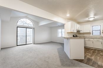 A spacious, empty room with a kitchenette and a large window with a view of a balcony.